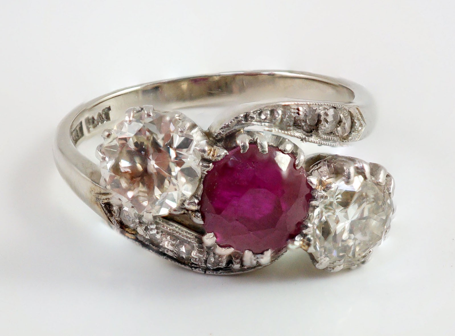 An 18ct white gold and platinum, two stone diamond and single stone synthetic? ruby set crossover ring, with diamond set shoulders
